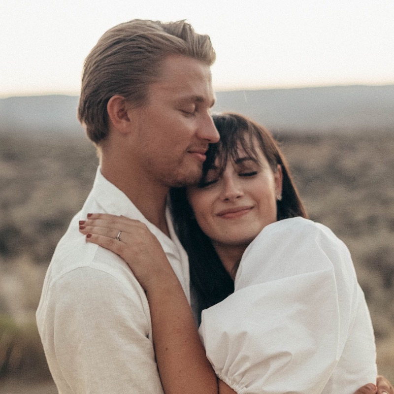 Ein Mann und eine Frau umarmen sich mit geschlossenen Augen und einem zufriedenen Grinser. Sie sind beide weiß gekleidet.