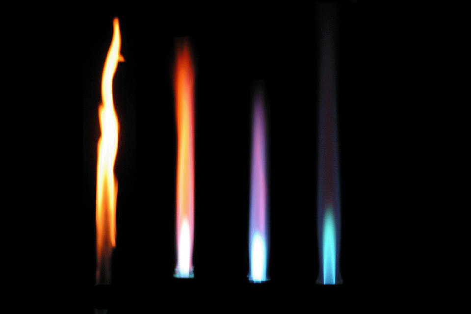 Vier Flammen, die den Unterschied zwischen geschlossener (rote unruhige Flamme) oder geöffneter Luftzuzuhr (ruhige, blaue Flamme) zeigen.