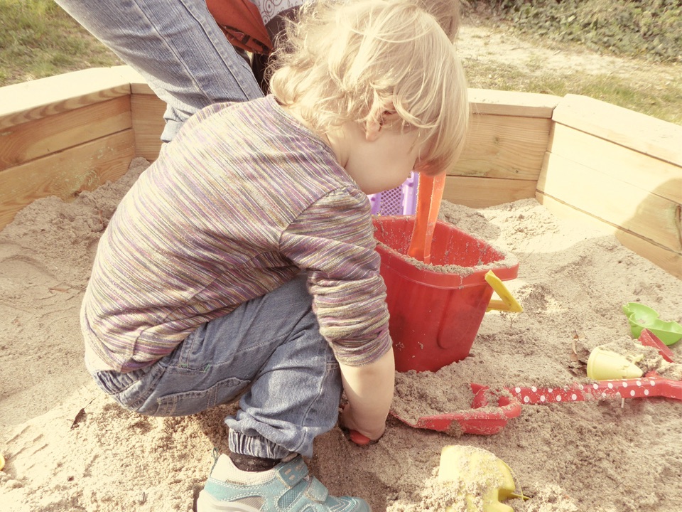 Man sieht ein kleines Kind beim Sandspielen.