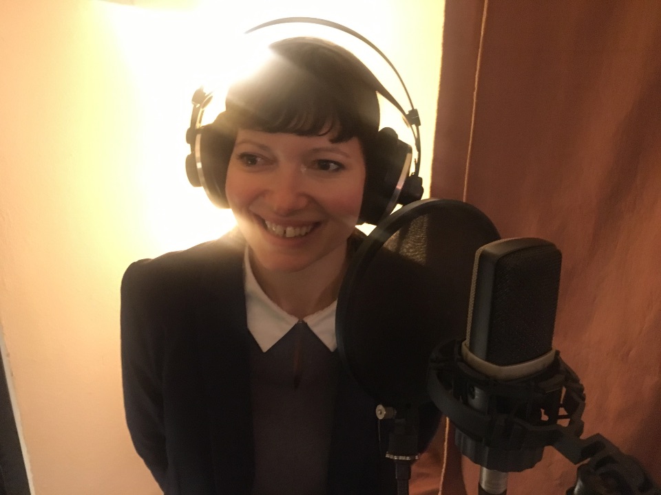 Man sieht Babsi Lippe, die die Feen für „The Tear“ gezeichnet hat, wie sie mit Kopfhörern vor einem Studiomikrofon steht, um den Feen im Spiel ihre Stimme zu verleihen.