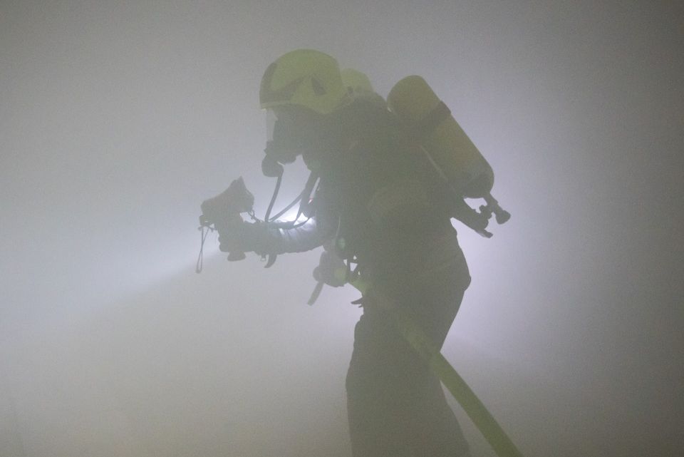 Ein Feuerwehrmann mit Feuerwehrhelm und Atemschutzmaske sowie einer Atemluftflasche am Rücken