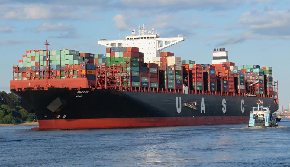 Ein rießiges Frachtschiff (mit der beschriftung UASCO) auf einem Gewässer mit vielen bunten hochgestapelten Containern