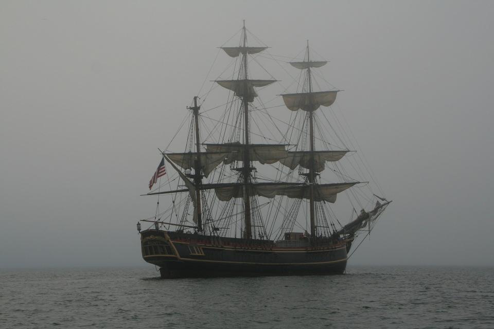 Ein großes Segelschiff mit hochgezogenen Segeln auf dem Meer in einer grauen nebligen Atmosphäre. 
