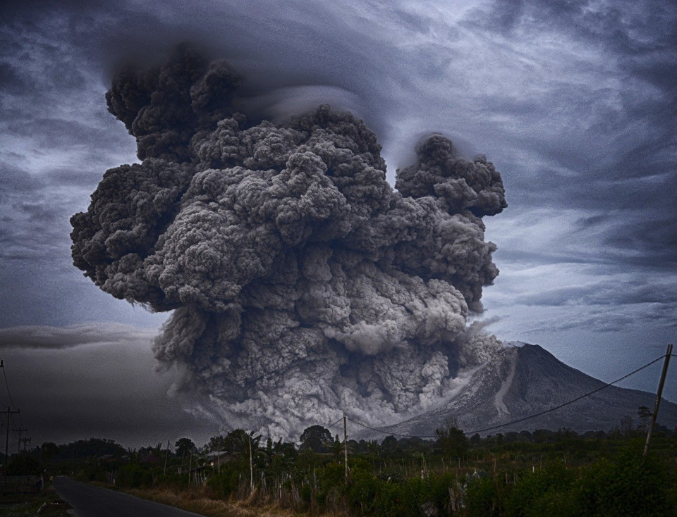 Bild eines Vulkanausbruchs mit imposanten großen, schwarzen Aschewolken und einem düsteren bewölkten Himmel 