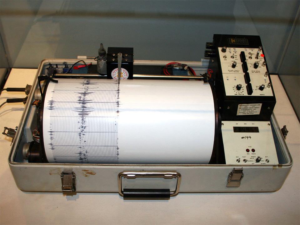 Ein Seismograf der ausschlägt - ersichtlich an den durch eine Nadel auf eine weiße Papierrolle aufgezeichneten Wellen.