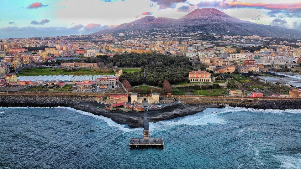 Eine Luftansicht von Neapel mit dem Vesuv im Hintergrund und der Küste im Vordergrund.