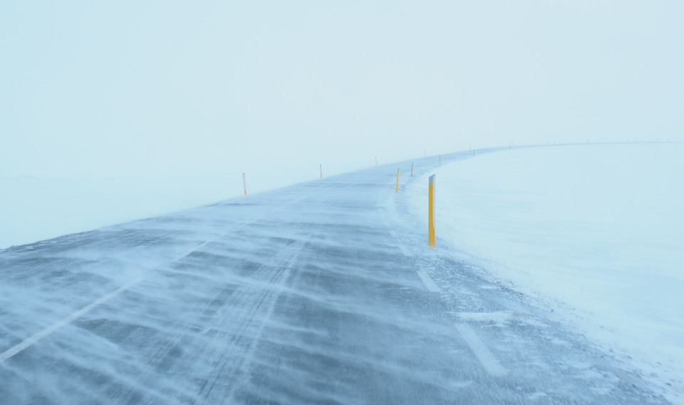 Eine verschneite Straße im Schneesturm, mit gelben Pfeilern als Sichthilfe.