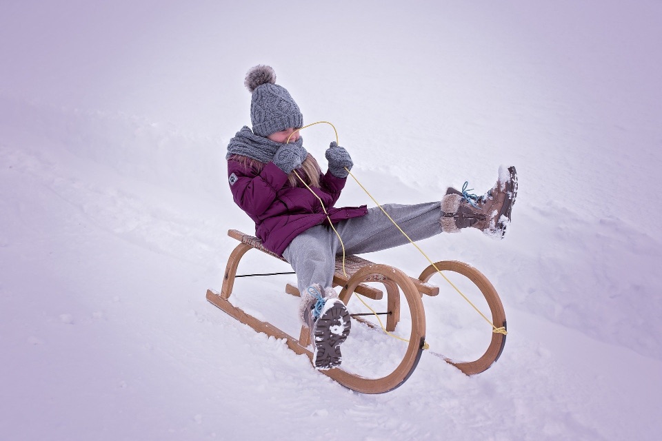 Ein Mädchen fährt mit einem Schlitten einen schneebedeckten Hang hinunter